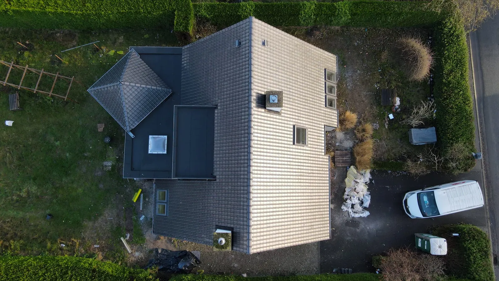 Bovenaanzicht van een woning met een nieuw pannendak, dakvensters, een plat dak met lichtkoepel en een uitbouw met piramidedak